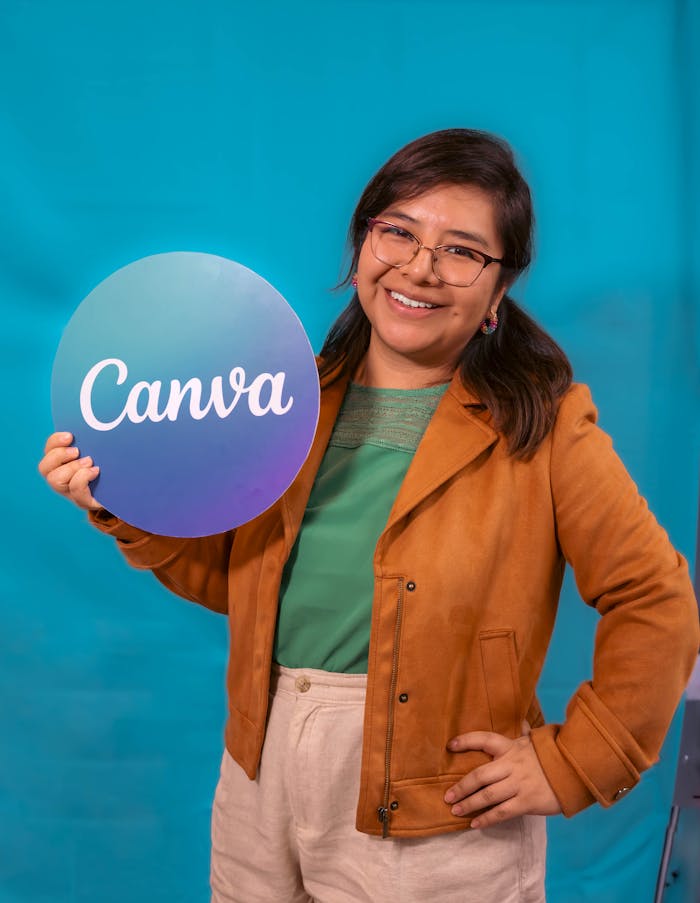 A smiling woman in a casual outfit holds a Canva sign, posing confidently against a vibrant blue backdrop.
